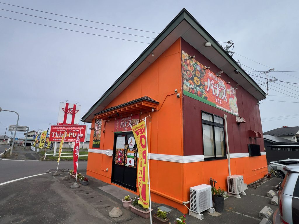 鮮やかなオレンジ色の建物と「NEW OPEN」ののぼりが並ぶ「パナス 水沢店」の店舗外観