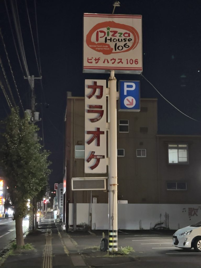 道路沿いに立つ「Pizza House 106」とカラオケの柱看板