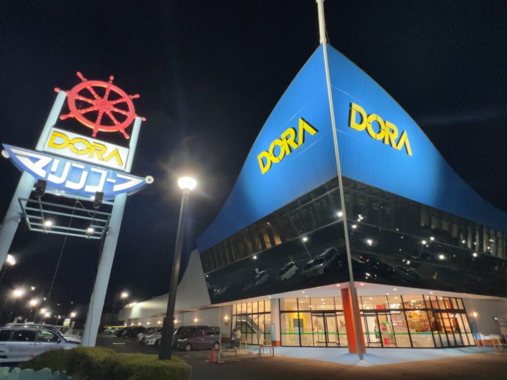 夜間にライトアップされた「いわて生協 マリンコープDORA」の建物と舵輪の看板