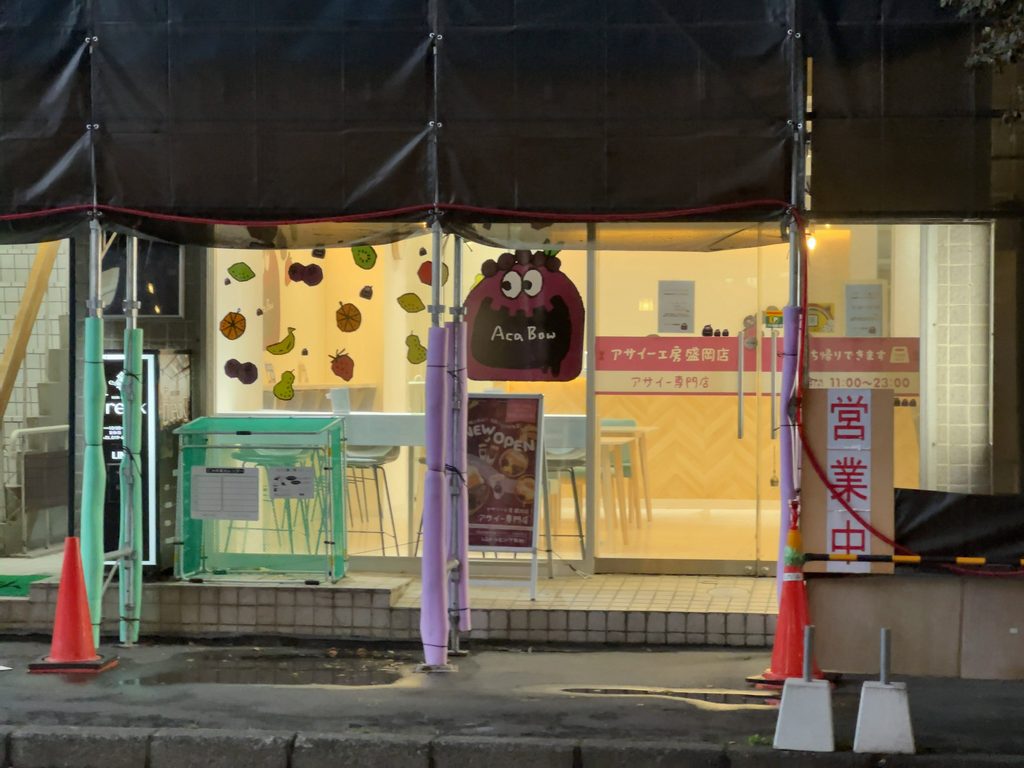 「アサイー工房 盛岡店」のピンクの看板とキャラクター「Aca Bow」が描かれた明るい店先