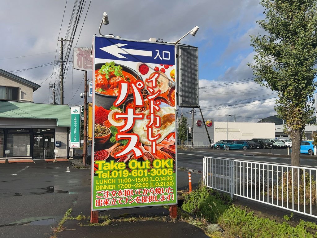 電話番号や営業時間、焼きたてナンの案内が書かれた「インドカレー パナス」の道路沿い看板