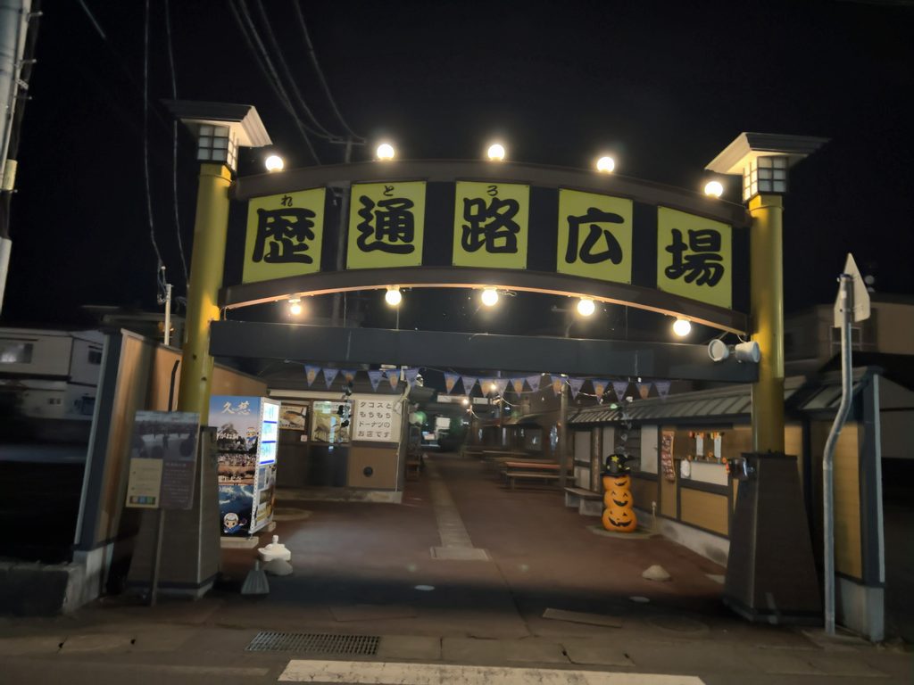 ハロウィンの飾りが施された夜の「歴通路広場」入口アーチと案内看板
