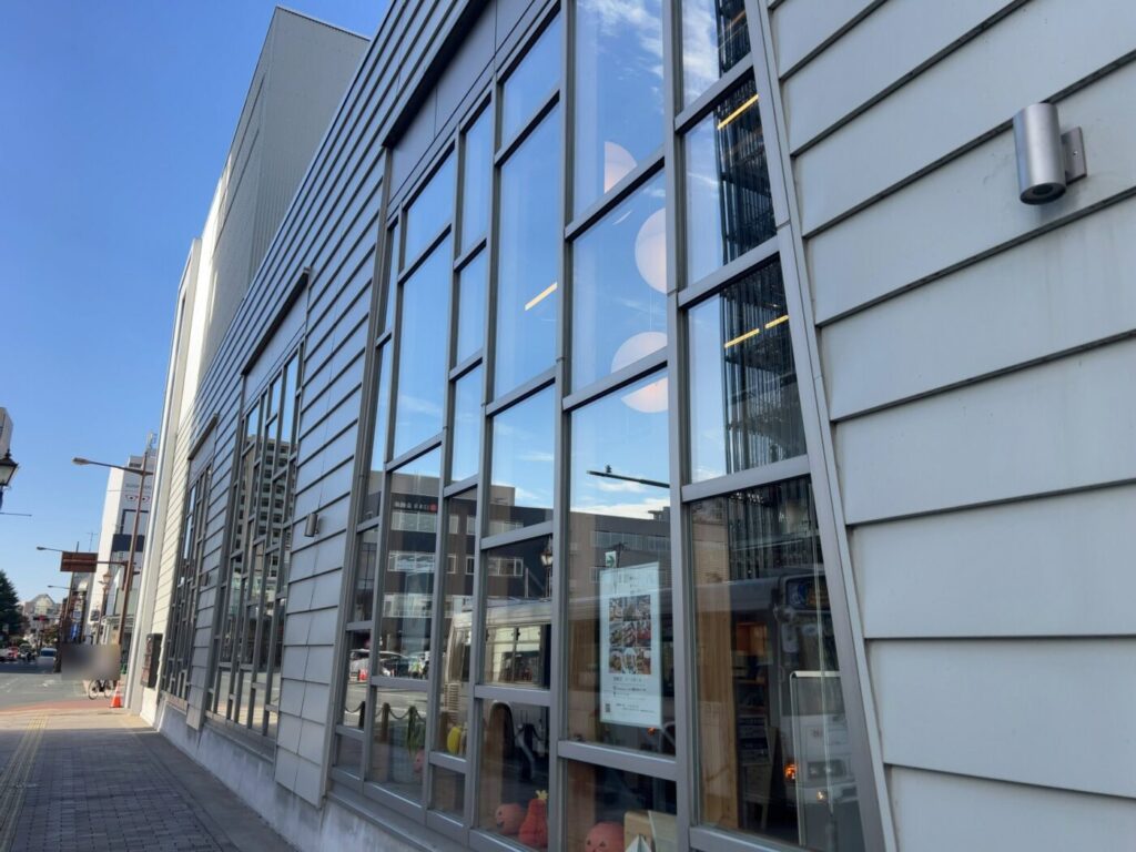 青空の下、ガラス張りの大きな窓が並ぶ白い建物の外壁と歩道